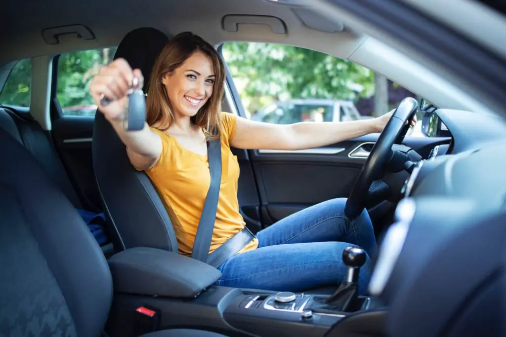 A woman happily showing off her car keys while sitting in the driver's seat