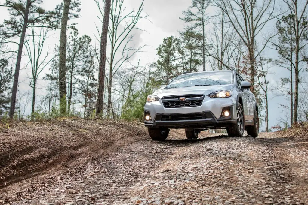 Silver Subaru on a dirt road in between trees
